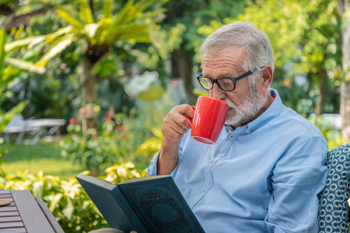 Elderly man drinking coffee while reading book