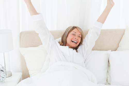 woman stretching her arms as she wakes up in bed