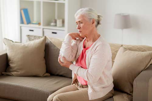 woman sitting on sofa holding her painful elbow