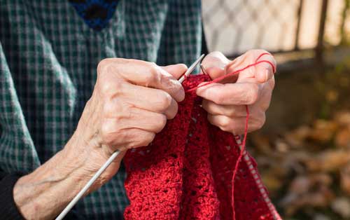 older woman knitting with red yarn