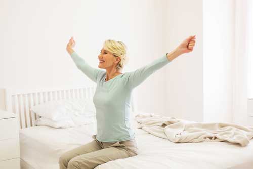 woman waking up, sitting up in bed stretching